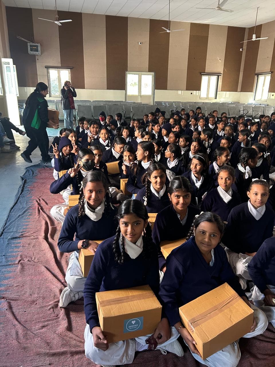 Schoolgirls holding EmpowerHer FlowKit boxes during a distribution