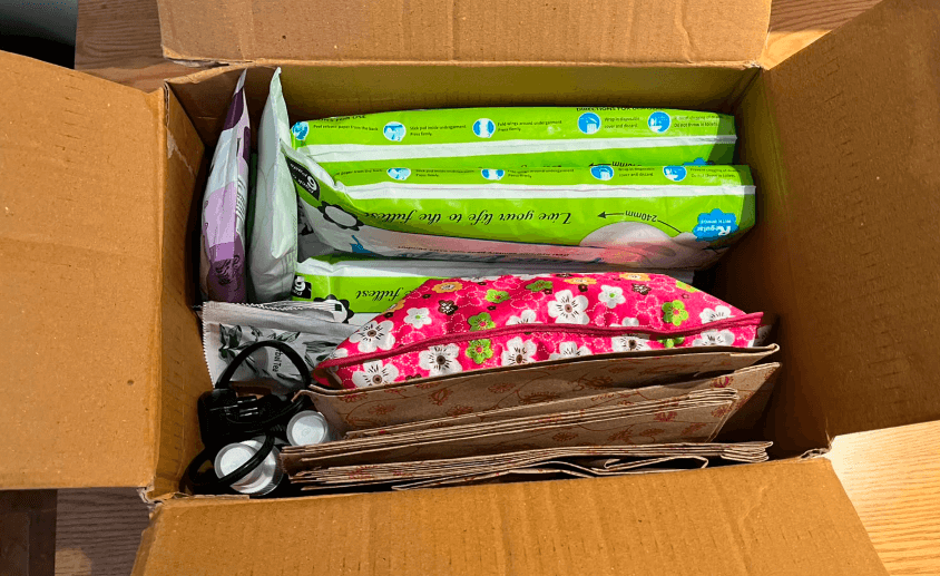 An open FlowKit showing sanitary pads, a floral pouch, disposal bags and a hot water bottle