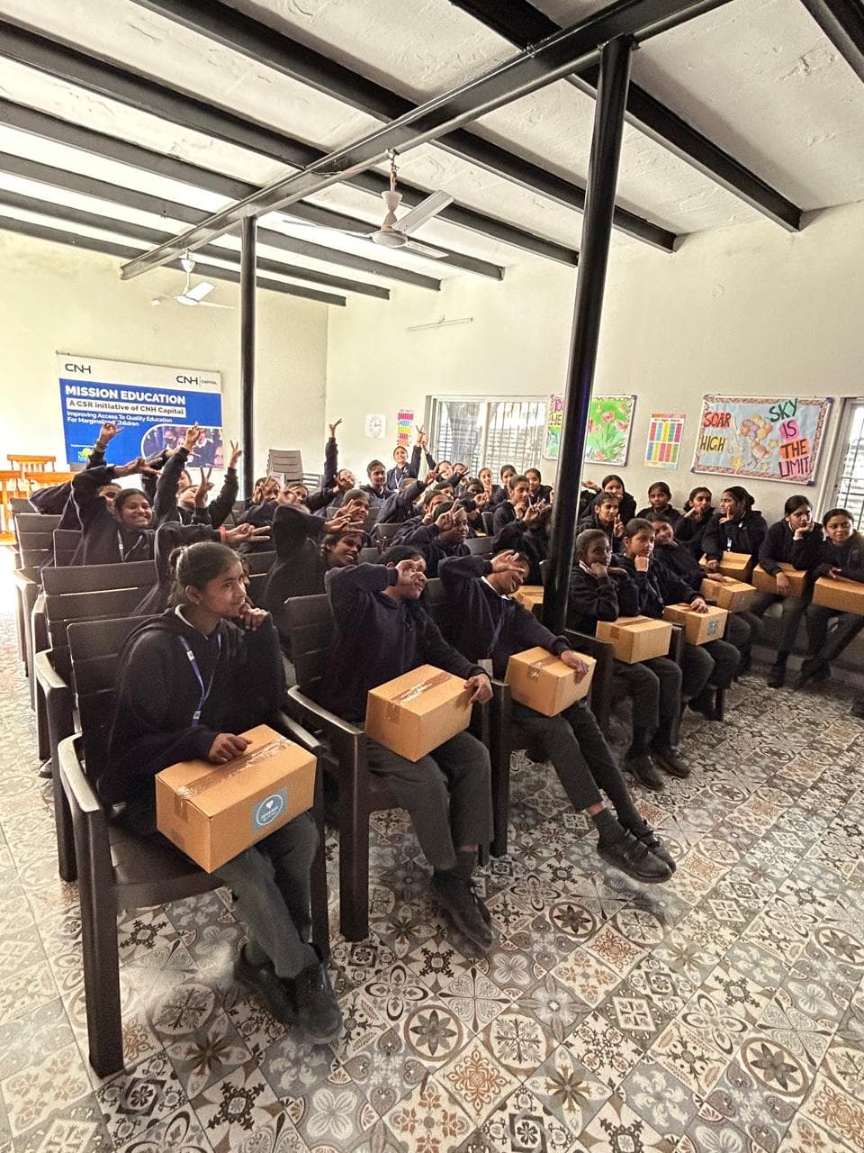 Girls in a classroom raising their hands with kit boxes
