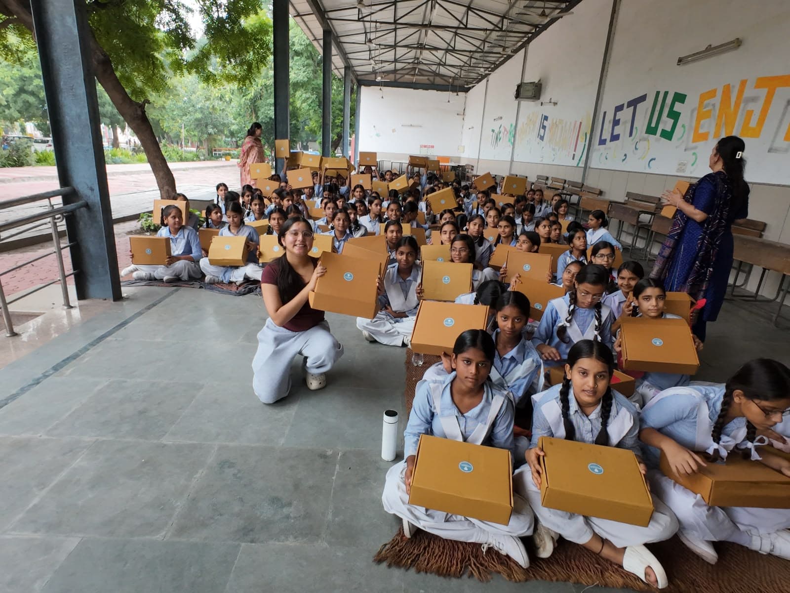 An EmpowerHer volunteer with schoolgirls holding their FlowKit boxes at a distribution